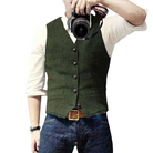 Mann in grüner Weste, weißem Hemd und blauer Jeans hält Kamera. Mode, Fotografie, Herrenbekleidung, Freizeitlook, stilvoll.