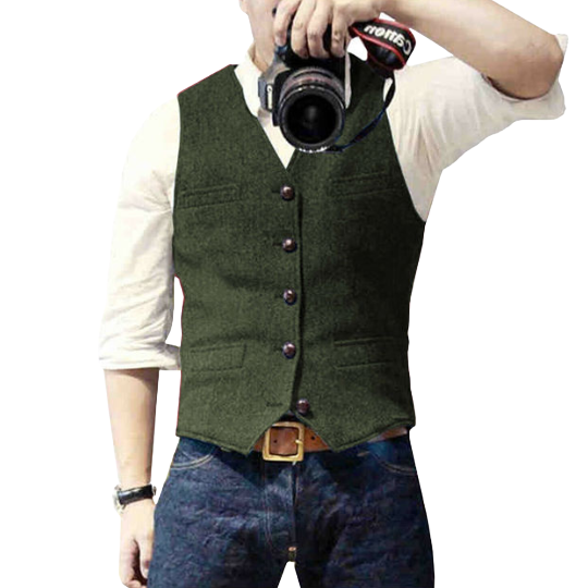 Mann in grüner Weste, weißem Hemd und blauer Jeans hält Kamera. Mode, Fotografie, Herrenbekleidung, Freizeitlook, stilvoll.