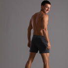 Mann in gestreifter Sportshorts, lächelnd, grauer Hintergrund, Fitnessmode, Activewear.