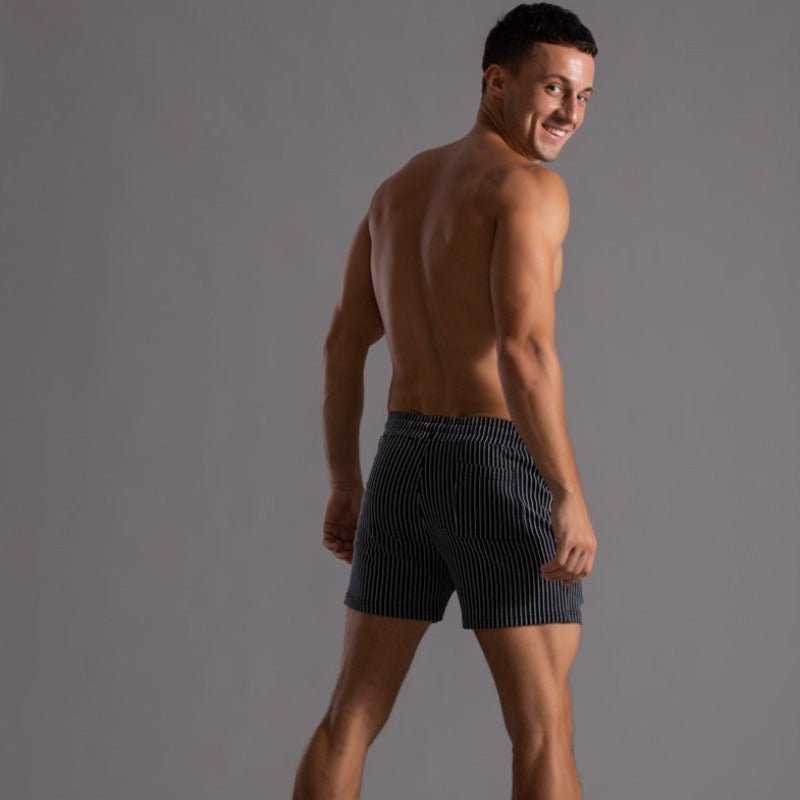 Mann in gestreifter Sportshorts, lächelnd, grauer Hintergrund, Fitnessmode, Activewear.