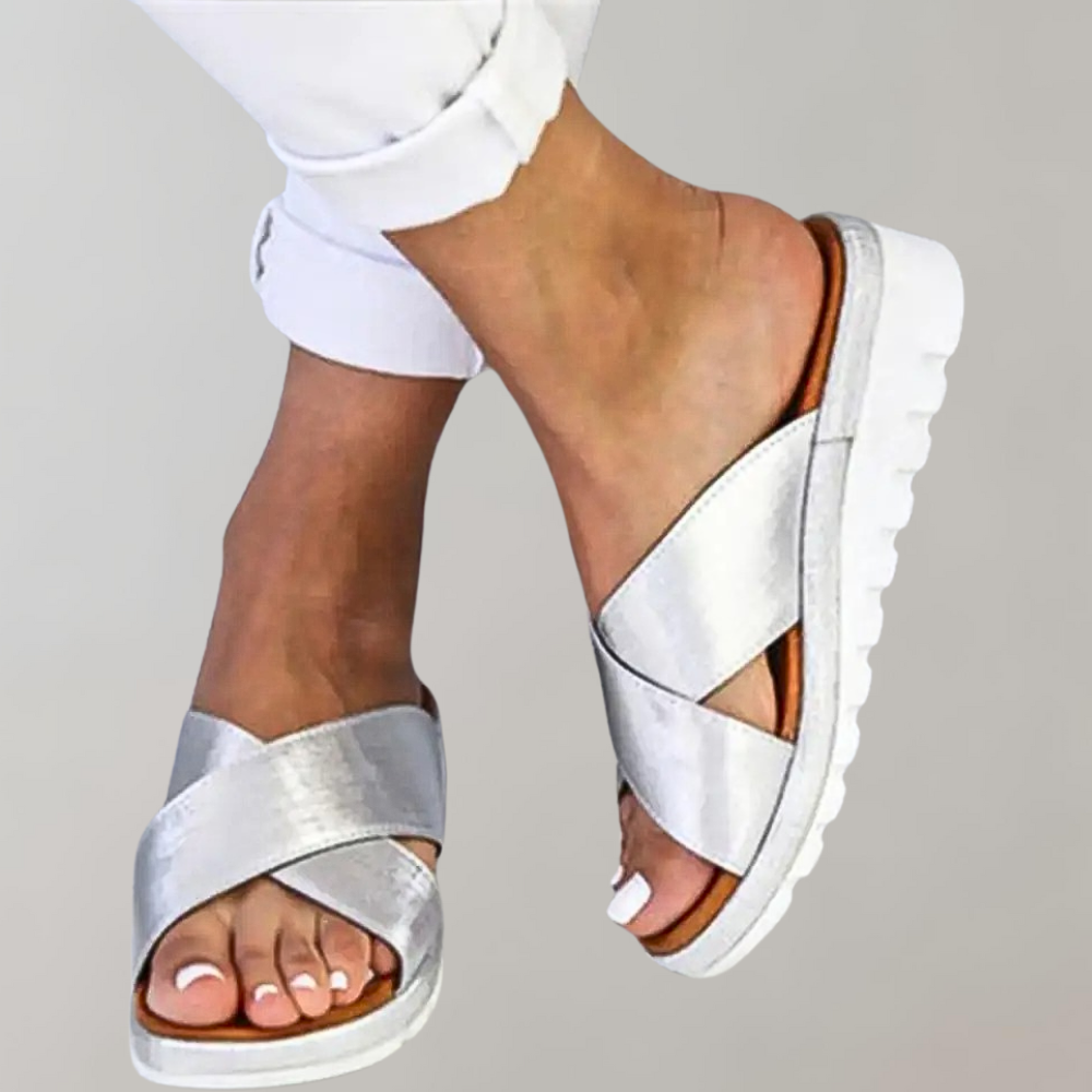Silberne Damen-Sandalen mit Kreuzriemen und weißer Sohle, ideal für Sommermode. Bequeme, stilvolle Schuhe für Freizeit und Alltag.
