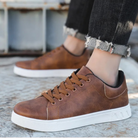 Braune Sneaker aus Lederimitat, lässig und modern, mit weißer Sohle. Perfekt für Herrenmode, Freizeitlook und urbanen Stil.
