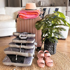 Reisekoffer mit Hut, Handtüchern, Packtaschen, rosa Sandalen und Zimmerpflanze im Wohnzimmer.