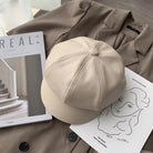 Beige Leder-Newsboy-Cap auf braunem Mantel, stilvoll und modern. Perfekt für Herbst und Winter. Trendige Damenmode, koreanischer Stil.