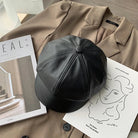 Schwarze Leder-Newsboy-Mütze auf beigem Mantel, stilvoll und modern. Perfekt für Herbst und Winter. Trendige Damenmode, koreanischer Stil.