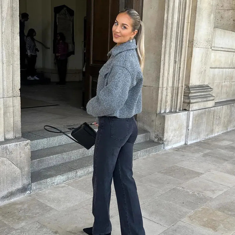 Frau in grauer Jacke und schwarzer Jeans vor historischer Architektur. Modetrend, Herbstmode, stilvolle Damenbekleidung, urbane Eleganz.