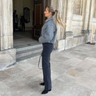 Frau in grauer Jacke und schwarzer Jeans vor historischer Architektur, eleganter Look, Herbstmode, stilvolle Kleidung, Streetstyle.