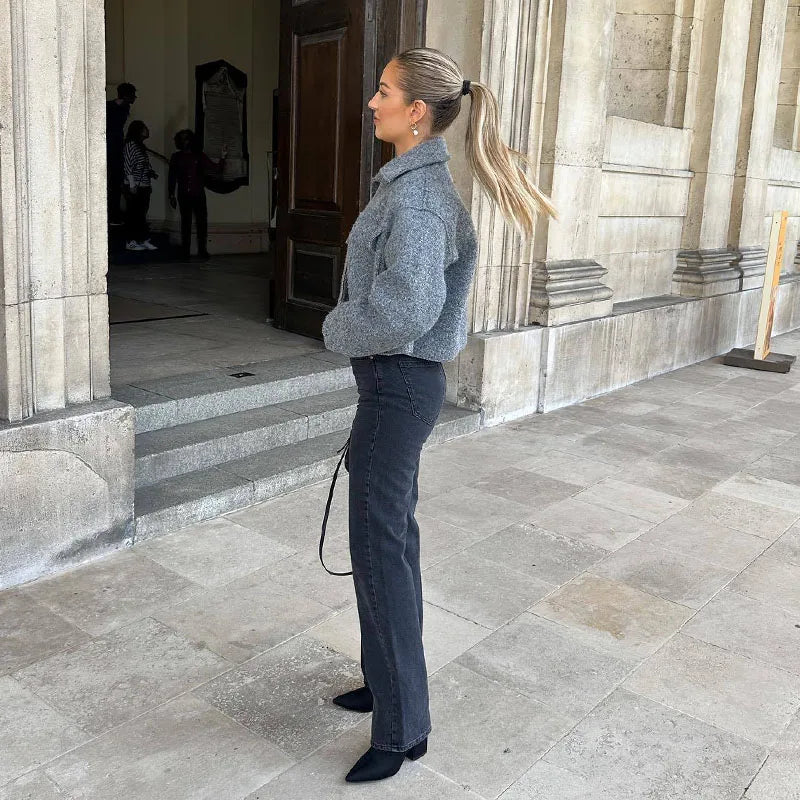 Frau in grauer Jacke und schwarzer Jeans vor historischer Architektur, eleganter Look, Herbstmode, stilvolle Kleidung, Streetstyle.