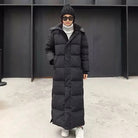 Langer schwarzer Daunenmantel für Damen, ideal für Wintermode. Stilvoll und warm, perfekt für kalte Tage. Kombiniert mit Mütze und Sonnenbrille.
