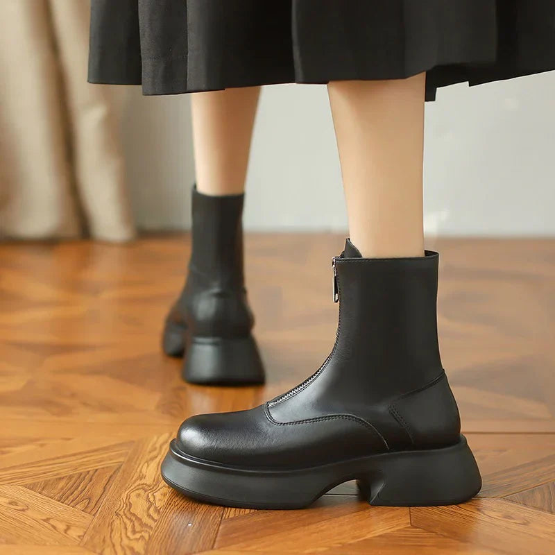 Schwarze Damenstiefel mit klobigem Absatz auf Holzboden. Modische, bequeme Stiefeletten, ideal für Herbst- und Winteroutfits.