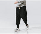 Schwarze Haremshose für Herren, lässig und bequem, ideal für Freizeit und Sport. Kombiniert mit grauem Sweatshirt und Adidas-Sneakern.