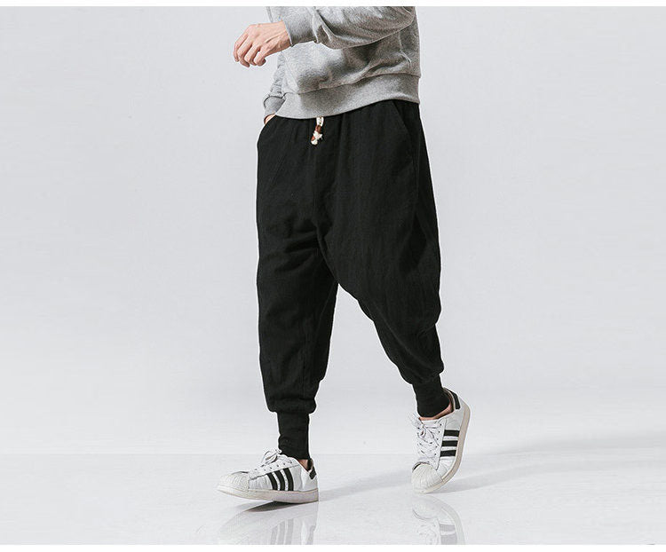 Schwarze Haremshose für Herren, lässig und bequem, ideal für Freizeit und Sport. Kombiniert mit grauem Sweatshirt und Adidas-Sneakern.