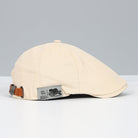 Beige Schiebermütze aus Baumwolle mit verstellbarem Lederriemen, stilvollem Design und hochwertigem Etikett, ideal für modische Outfits.