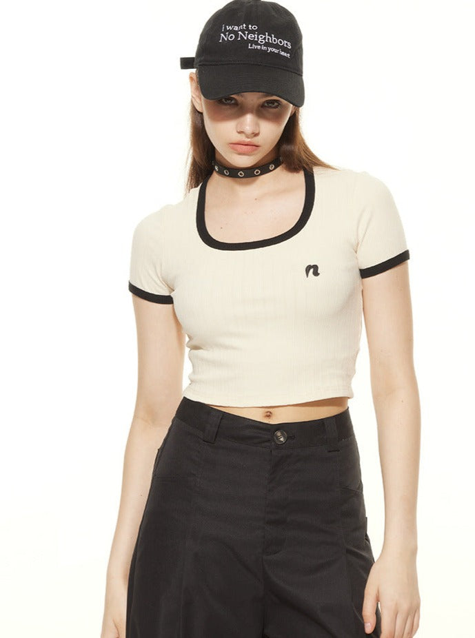 Frau trägt schwarzes Cap mit Aufschrift, weißes Crop-Top und schwarze Hose. Modetrend, Streetwear, lässiger Stil, urbaner Look, Damenmode.