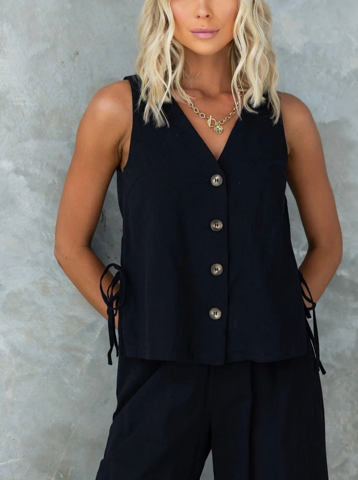 Ärmellose schwarze Damenweste mit Knopfleiste und seitlichen Schleifen, ideal für elegante und lässige Outfits. Perfekt für den modernen Look.