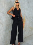 Elegantes Damen-Outfit: Schwarze ärmellose Weste und weite Hose, ideal für Sommermode. Perfekt kombiniert mit Sonnenbrille und Sandalen.