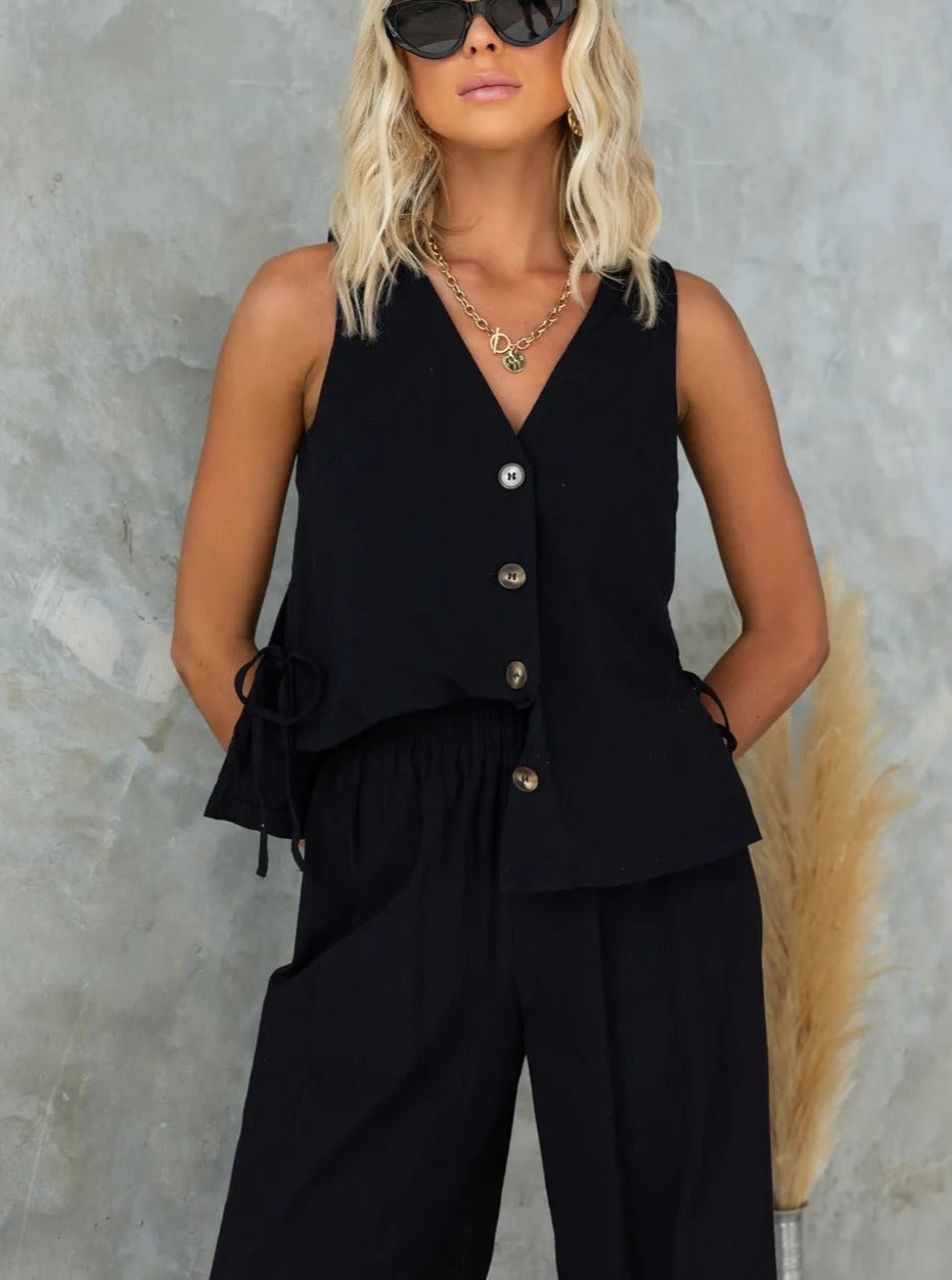 Elegantes Damen-Outfit: Schwarze ärmellose Bluse mit Knöpfen, kombiniert mit passender Hose. Perfekt für stilvolle Sommermode und Freizeitlooks.