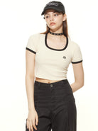Frau in modischem Crop-Top und schwarzer Hose, trägt eine Baseballkappe und Choker. Trendige Streetwear, lässiger Look, urbaner Stil.