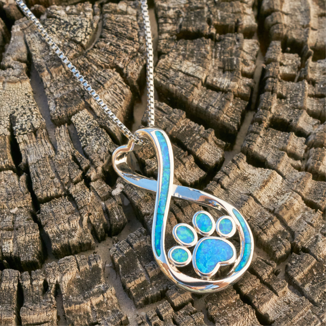 Opal Infinity Love Pfoten Halskette auf Holz, elegantes Schmuckstück mit blauem Opal, ideal für Tierliebhaber, modisches Accessoire.