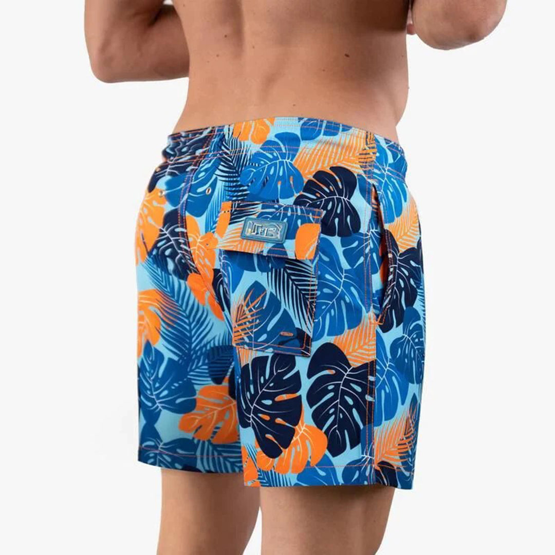 Mann in blauer und orangefarbener Badehose mit tropischem Blattmuster von hinten.
