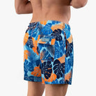 Mann in blauer und orangefarbener Badehose mit tropischem Blattmuster von hinten.