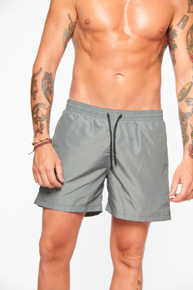 Mann in grauer Badehose mit Tattoos auf weißem Hintergrund. Sommermode, Herrenbadebekleidung, stilvolle Badeshorts, Strandoutfit.