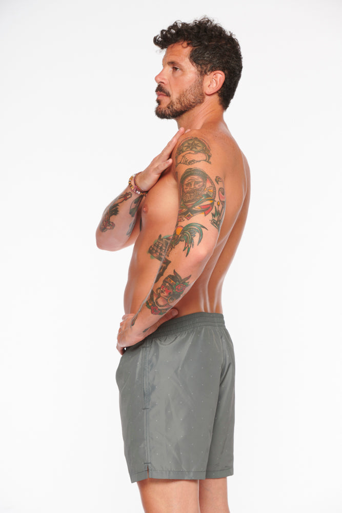 Mann in grauer Badehose, seitlich, mit tätowierten Armen. Sommermode, Herrenbadebekleidung, stilvolle Badeshorts, Freizeitlook.