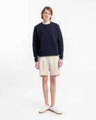 Junger Mann in lässigem Outfit: Dunkler Pullover, beige Shorts, weiße Sneaker. Minimalistischer Stil, moderne Herrenmode, Sommerlook.
