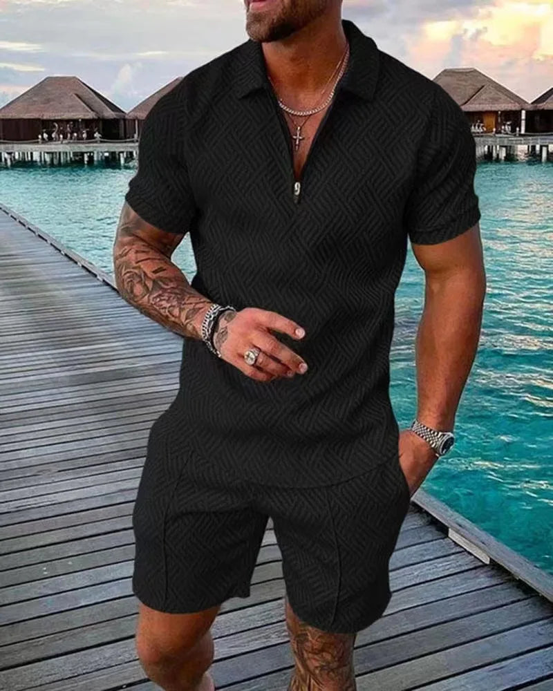 Mann in schwarzem, gemustertem Kurzarm-Overall auf Holzsteg am Meer. Sommermode, Herrenbekleidung, stilvoller Look, Urlaubsoutfit.