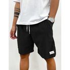 Mann trägt schwarze Shorts mit weißem Kordelzug und T-Shirt, Armbanduhr, lässige Sommermode.