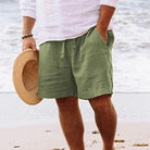 Grüne Leinen-Shorts für Herren am Strand, kombiniert mit weißem Hemd und Strohhut. Perfekt für Sommermode, Strandbekleidung, lässiger Stil.