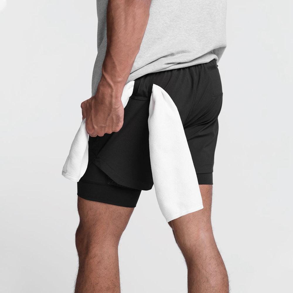 Mann in schwarzer Sporthose mit weißem Handtuch, Fitnessbekleidung, Rückansicht.