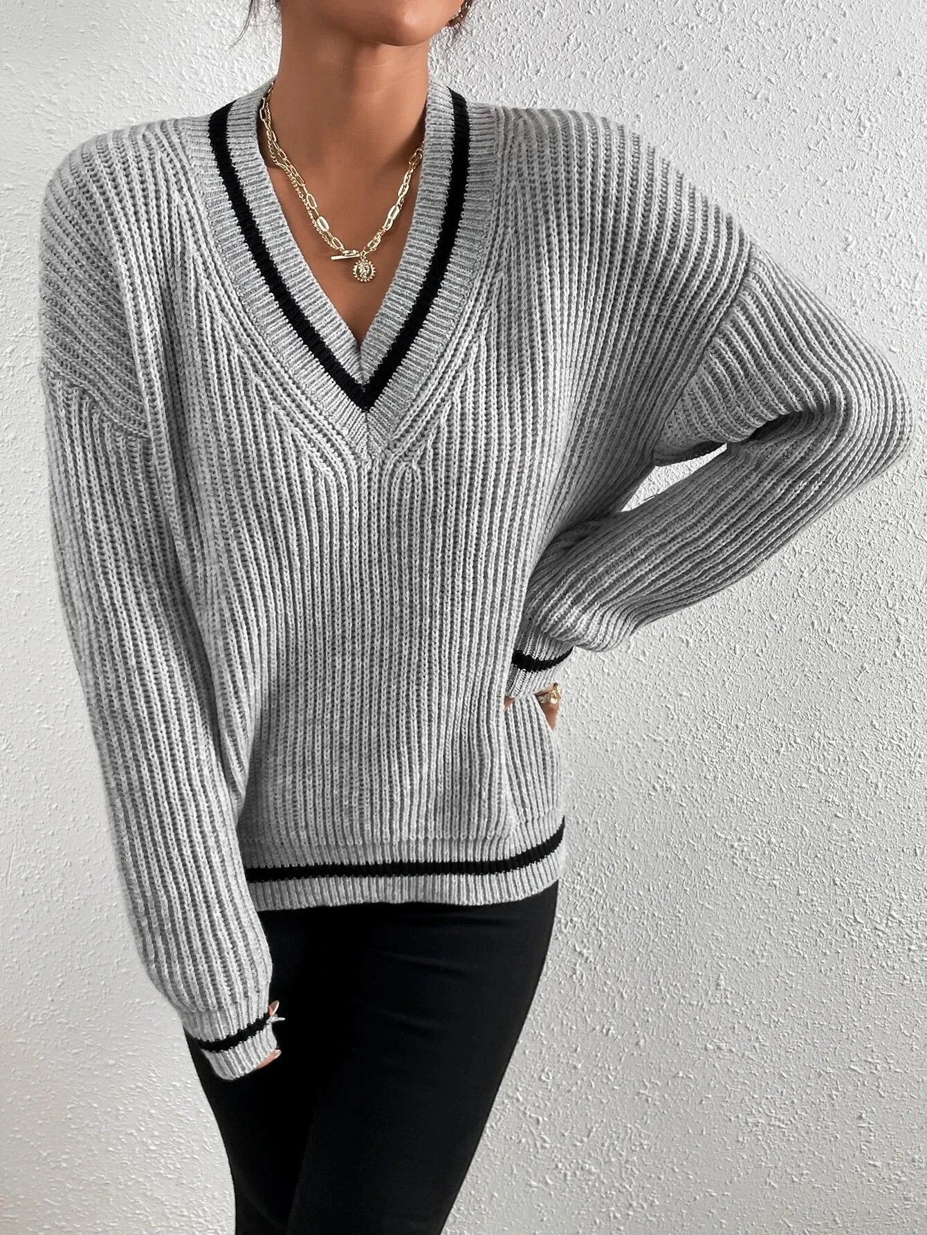 Grauer Strickpullover mit V-Ausschnitt, schwarz-weißen Streifen und lässigem Schnitt. Perfekt für Herbstmode und stilvolle Outfits.