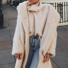 Flauschiger, cremefarbener Kunstpelzmantel kombiniert mit einem Rollkragenpullover und Jeans. Trendige Wintermode für stilvolle Damen.