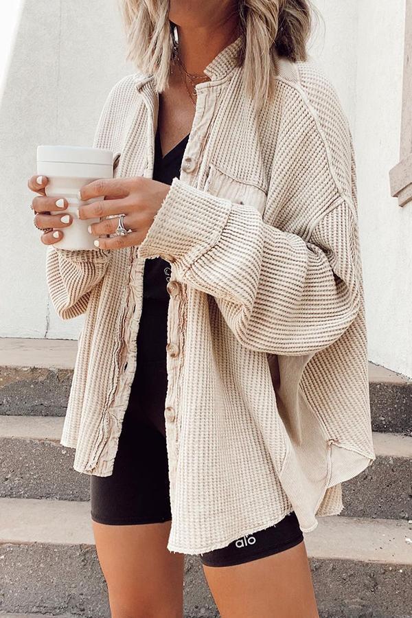 Frau in beigem Strickhemd hält weißen Kaffeebecher. Modetrend, lässiger Stil, Herbstmode, Damenbekleidung, Streetwear, gemütlicher Look.