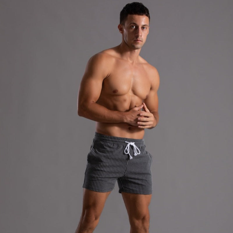 Mann in gestreifter Badeshorts, muskulös, vor grauem Hintergrund. Sommermode, Herrenbekleidung, Strandoutfit, Fitness, Freizeitlook.