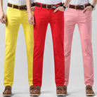 Drei Herren-Chinos in Gelb, Rot und Rosa, kombiniert mit braunen Lederschuhen. Modische, farbenfrohe Hosen für stilvolle Outfits.