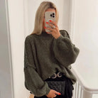 Frau in grünem Strickpullover, hält Smartphone, trägt schwarze Tasche. Modetrend, Herbstmode, Damenbekleidung, stilvoller Look.