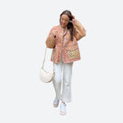 Frau in modischer, gesteppten Jacke mit Blumenmuster, weißer Hose und Sneakers. Trendige Herbstmode, Streetstyle, lässiger Look.
