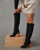 Damenmode: Schwarze Overknee-Stiefel aus Wildleder mit Blockabsatz, kombiniert mit einem cremefarbenen Strickkleid. Elegante Herbstmode.