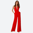 Frau im eleganten roten Jumpsuit, ärmellos, mit weitem Bein, vor neutralem Hintergrund.