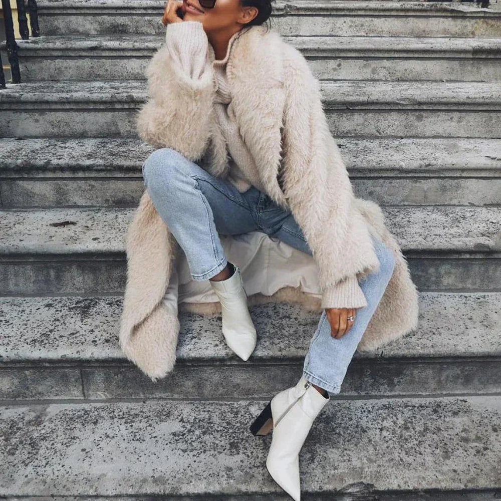 Frau in modischem, flauschigem Mantel, kombiniert mit blauen Jeans und weißen Stiefeletten. Trendige Herbstmode, stilvoll und elegant.