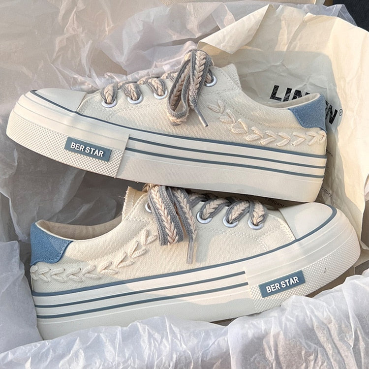 Weiße Leinenschuhe mit blauen Akzenten, dicker Sohle und geflochtenen Details. Trendige Sneaker, ideal für Casual-Outfits und Streetwear.
