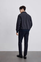 Mann in eleganter, dunkelblauer Bomberjacke und Hose, steht vor grauem Hintergrund. Stilvolle Herrenmode, zeitloses Design, moderne Eleganz.