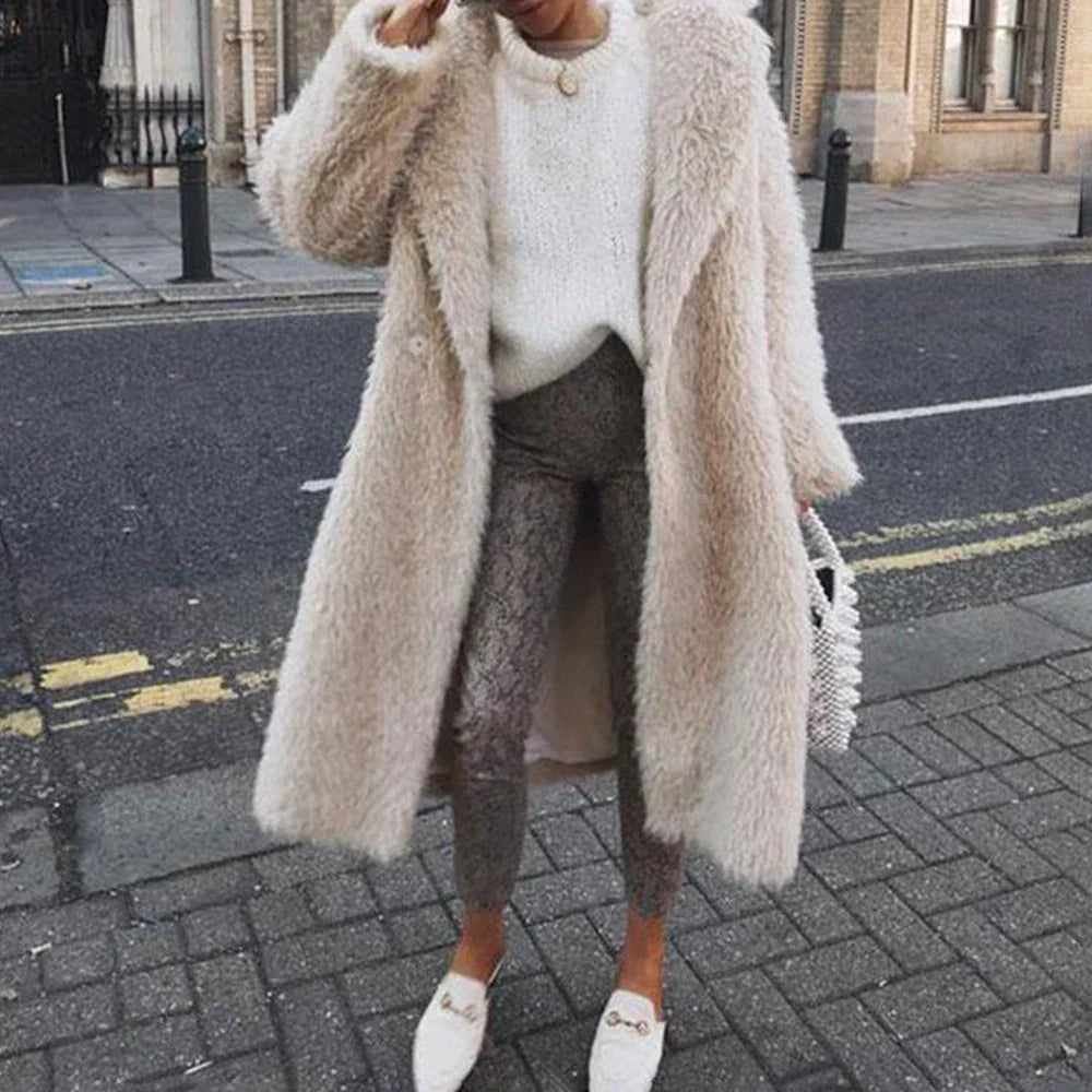 Frau in stilvollem, langem, beigem Kunstpelzmantel, kombiniert mit weißem Pullover und eleganten Schuhen. Perfekt für Wintermode und Streetstyle.