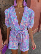 Farbintensiver Jumpsuit mit abstraktem Muster, V-Ausschnitt und Taillengürtel. Perfekt für Sommermode, trendige Damenbekleidung, stilvolle Outfits.