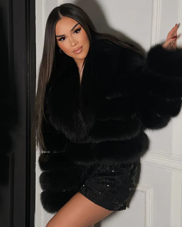 Frau in elegantem, schwarzem Pelzmantel, posiert stilvoll vor weißer Wand. Mode, Luxus, Winterbekleidung, glamouröser Look, Damenmode.