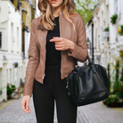 Frau in brauner Lederjacke und schwarzer Hose mit schwarzer Handtasche auf gepflasterter Straße. Modetrend, Damenmode, stilvolle Outfits.