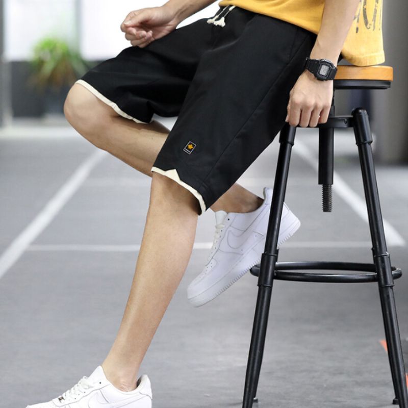 Mann in schwarzen Sportshorts und weißen Sneakers auf Hocker, Sommermode, Fitnessbekleidung.