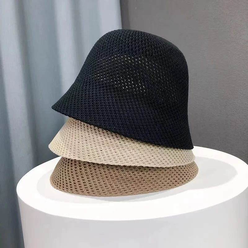 Drei gestrickte Sommer-Bucket-Hüte in Schwarz, Beige und Creme auf weißem Podest. Atmungsaktiv, faltbar, ideal für Strand und Outdoor.